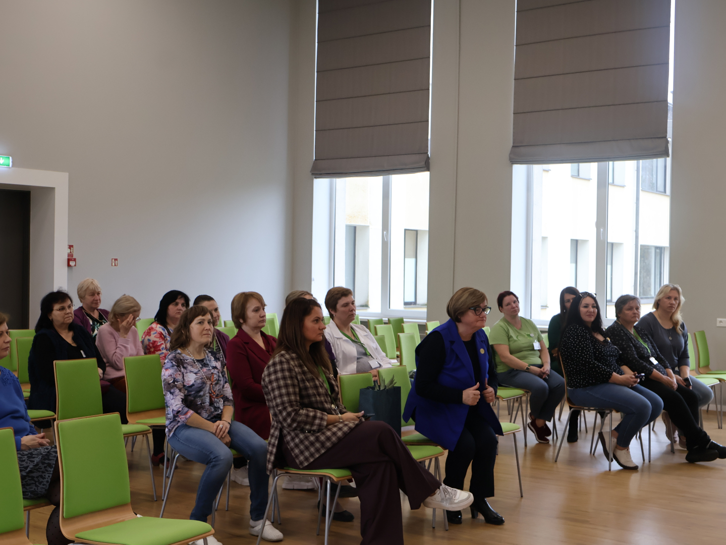 Zāles priekšā runā mākslas terapeite. Zālē sēž klausītāji