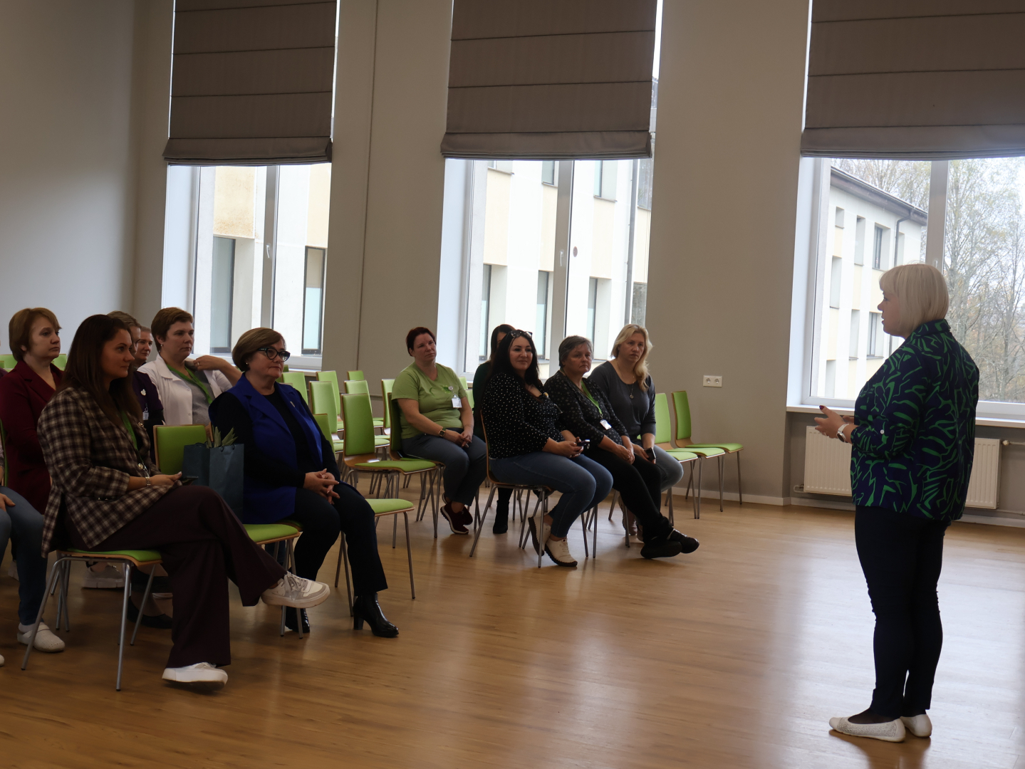 Zāles priekšā runā mākslas terapeite. Zālē sēž klausītāji