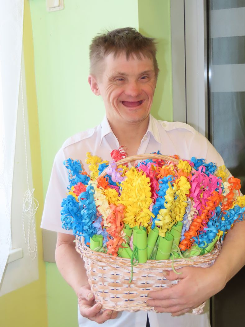 Smaidīgs iedzīvotājs ar lielu grozu, kurā sakārtoti krāsaini papīra ziedi