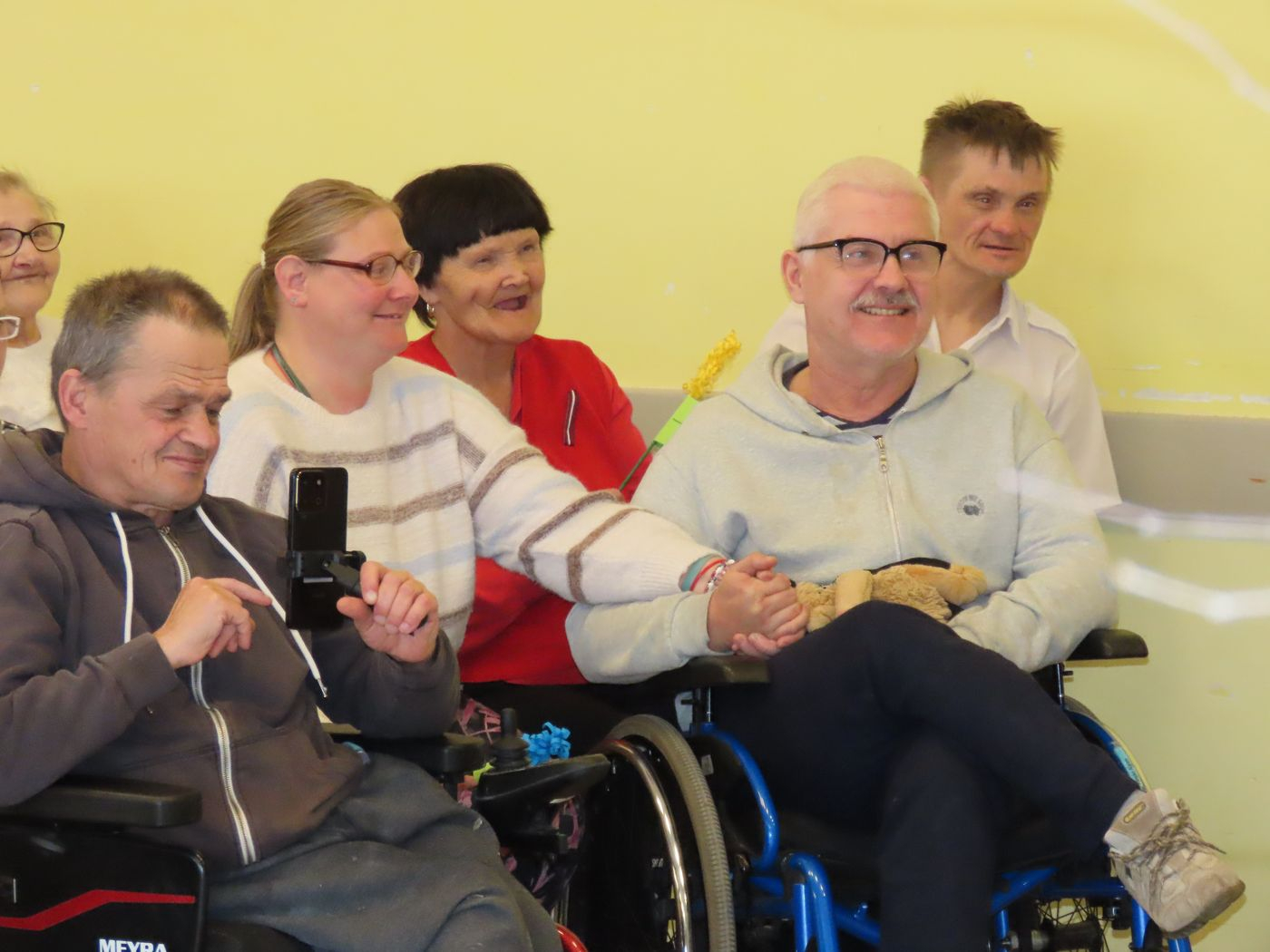 Skatītāi, iedzīvotāji gan krēslos, gan ratiņkrēslos. visi seši smaida