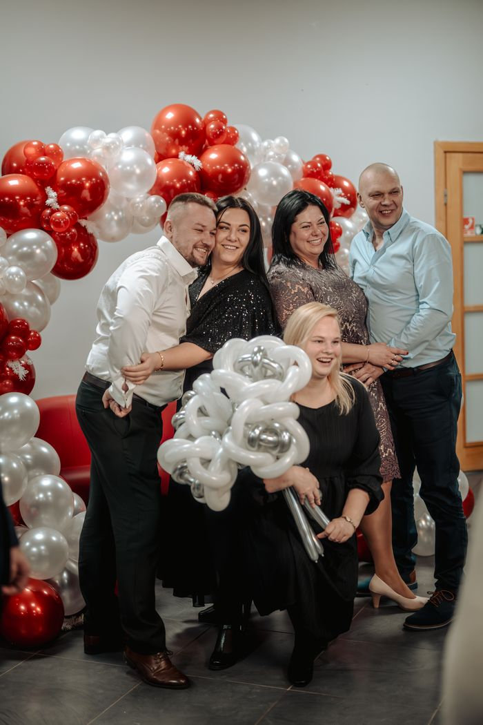Iestādes darbinieki fotografējas pie sarkanu un baltu balonu arkas