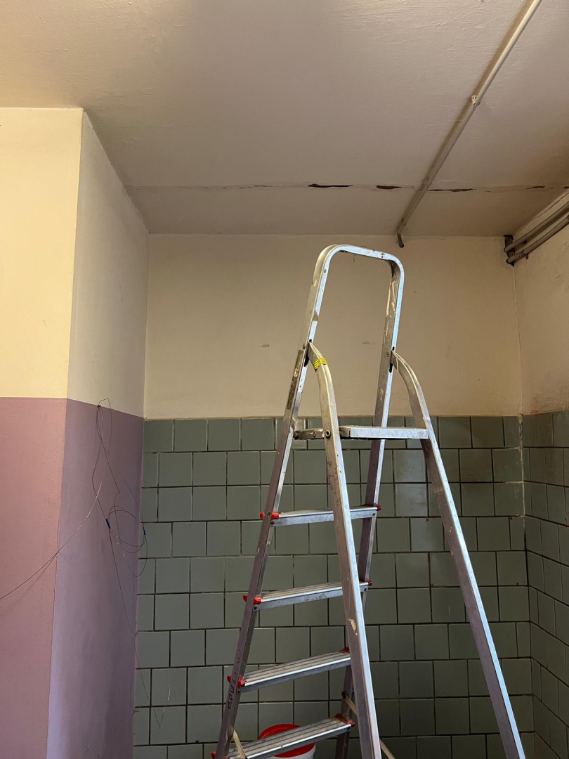Telpa pirms remonta veikšanas. Netīras sienas baltā un lillā krāsā, blāvi zilas flīzes.