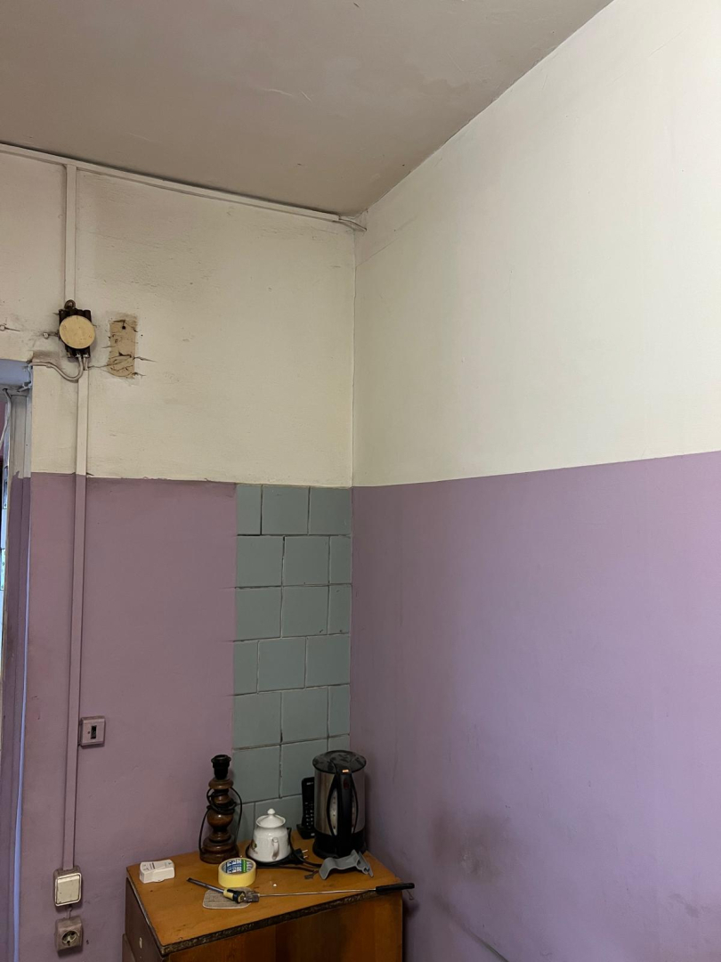 Telpa pirms remonta veikšanas. Netīras sienas baltā un lillā krāsā, blāvi zilas flīzes.