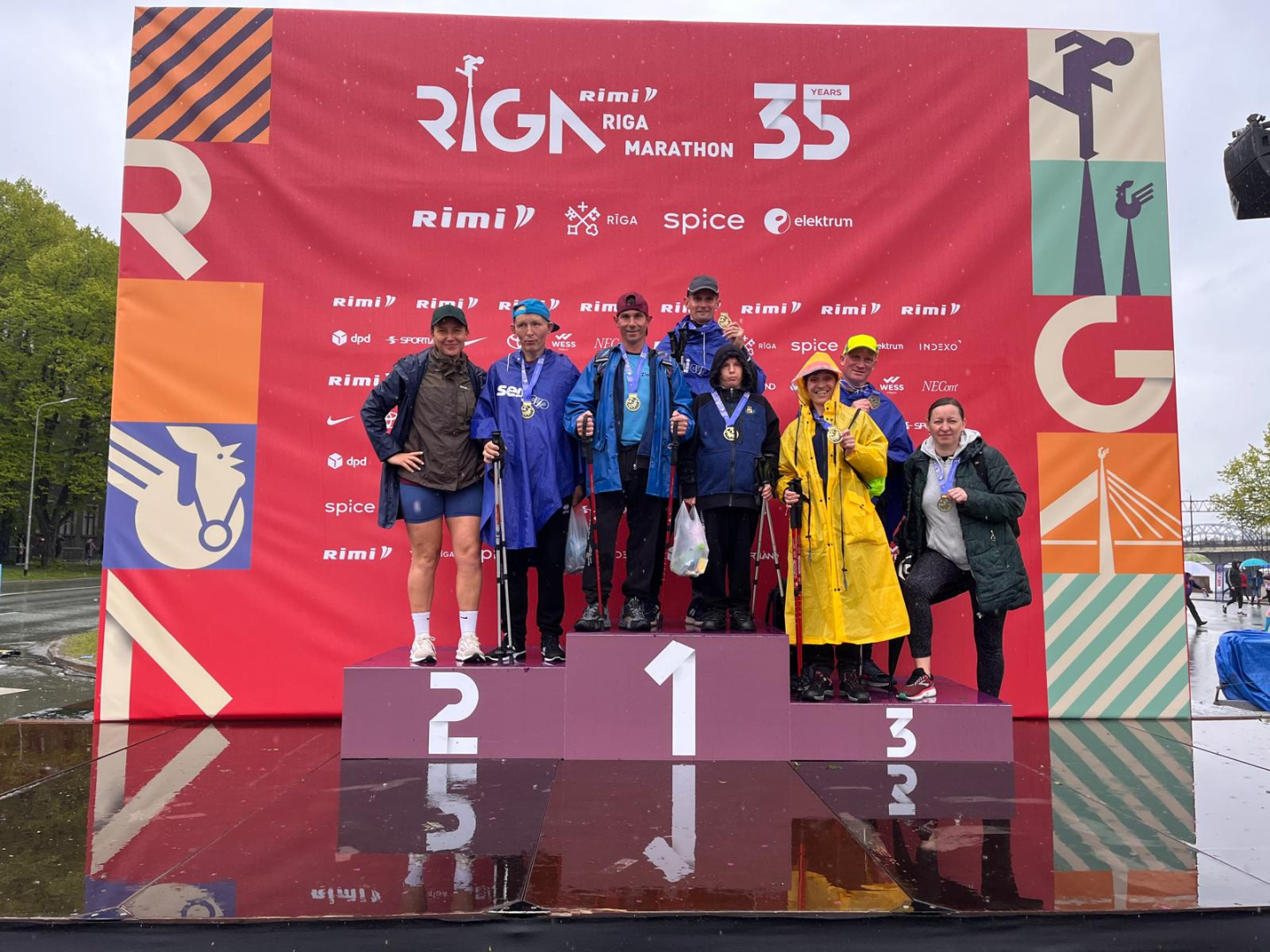 Rimi Rīgas maratona dalībnieki uz goda pjedestālapēc distances veikšanas. Smaidīgi, ar medaļām