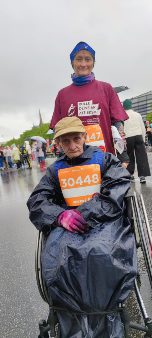 Maratona dalībnieks ratiņkrēslā ar darbinieci pirms distances veikšanas