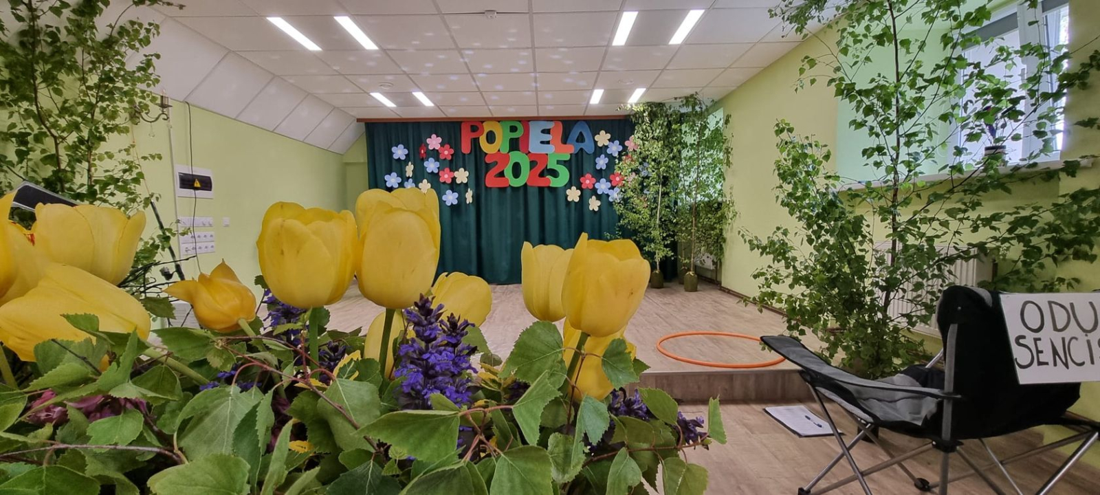 Skats uz pasākuma skatuvi. Izrātāta ar lieliem burtiem POPIELA 2025