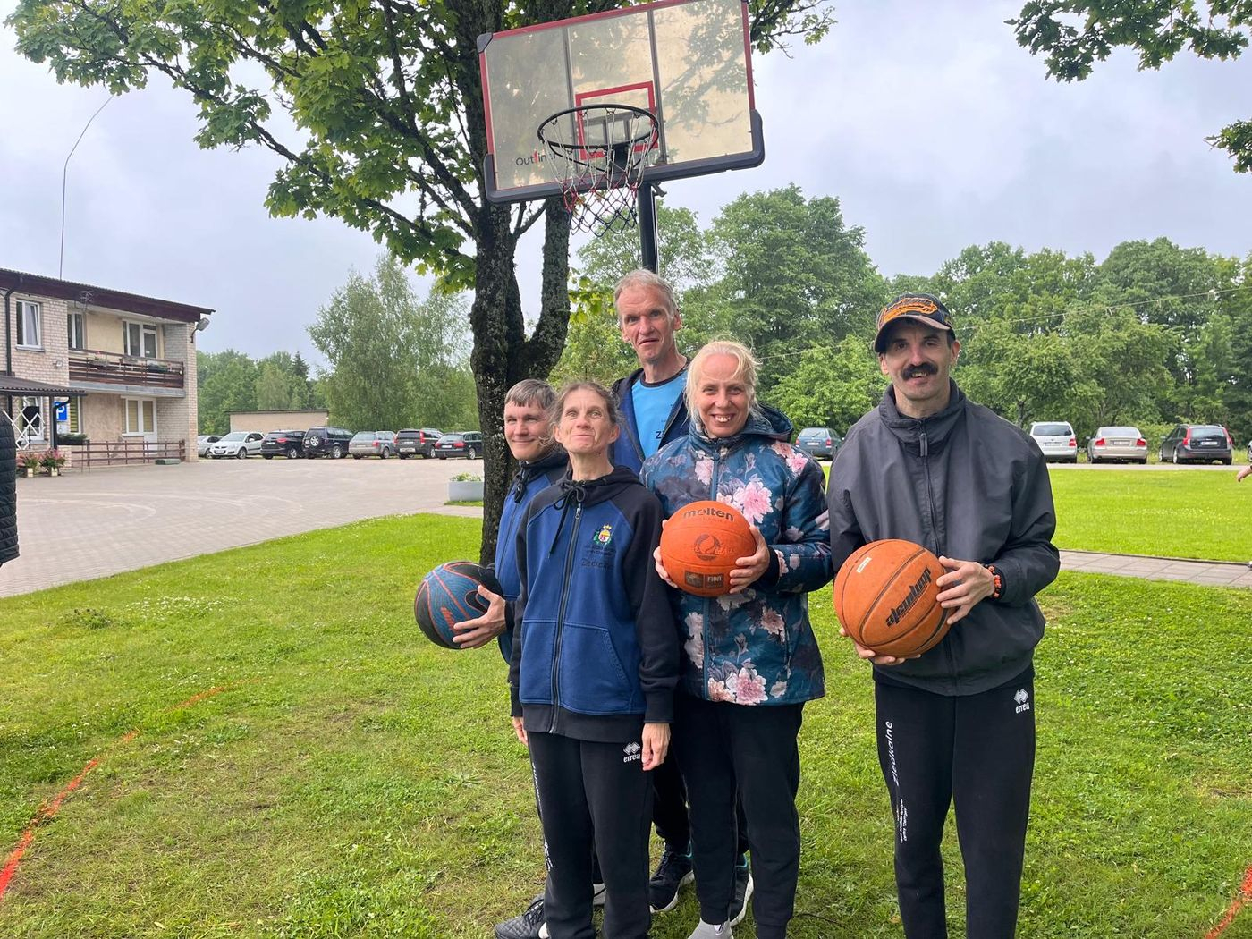 Pieci dalībnieki pie basketbola groza ar basketbola bumbām rokās