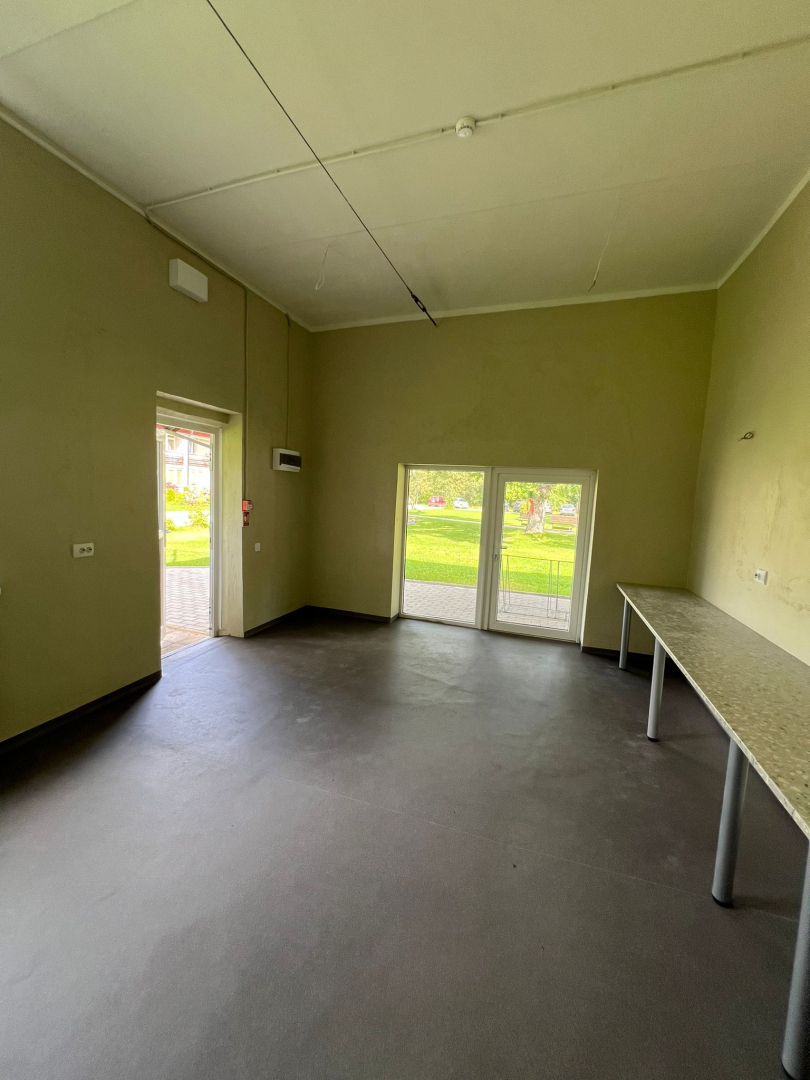 Attēls ar garāžas telpas stāvokli pēc remonta. Skaistas svaigas sienas gaišā krāsojumā, grīdas segums tumšs, gar sienu galda virsmas, plašas durvis