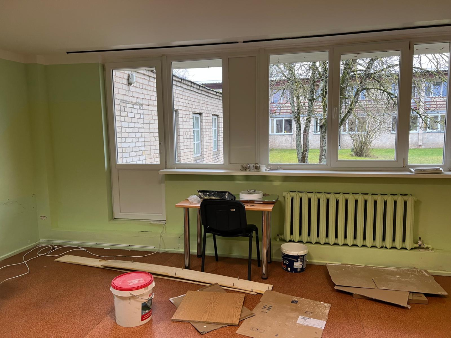 Telpa pirms remonta veikšanas. Nolietojušās sienas blāvi gaišā krāsā. Pie sienas remontdarbu materiāli, krāsas un citi