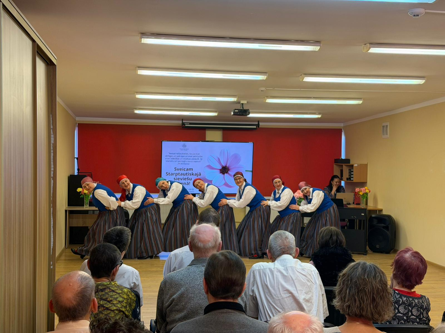 Redzams kā iestādes iedzīvotāji vēro koncertu, kā dāmas tautastērpos dejo