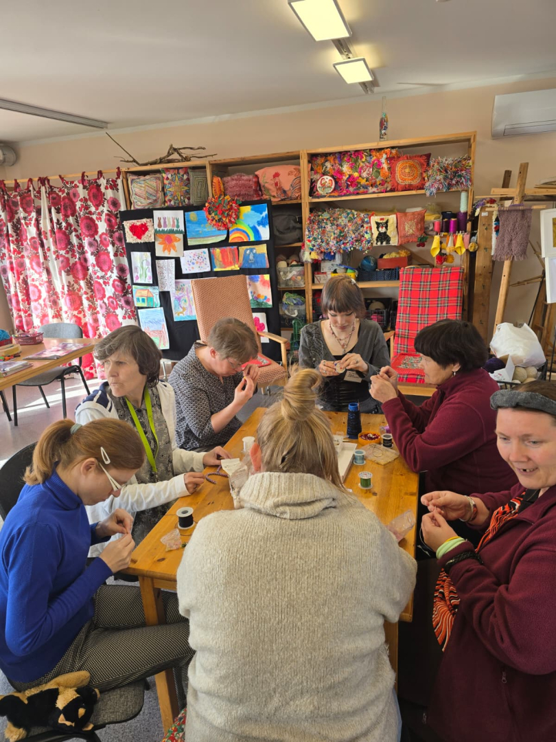 Rokdarbu nodarbība, jauniete un iedzīvotāji sēž pie galda un darbojas