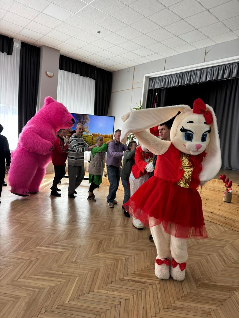 Cilvēki dejo ar diviem cilvēkiem, kuri tērpušies lielajos zaķa un lāča kostīmos