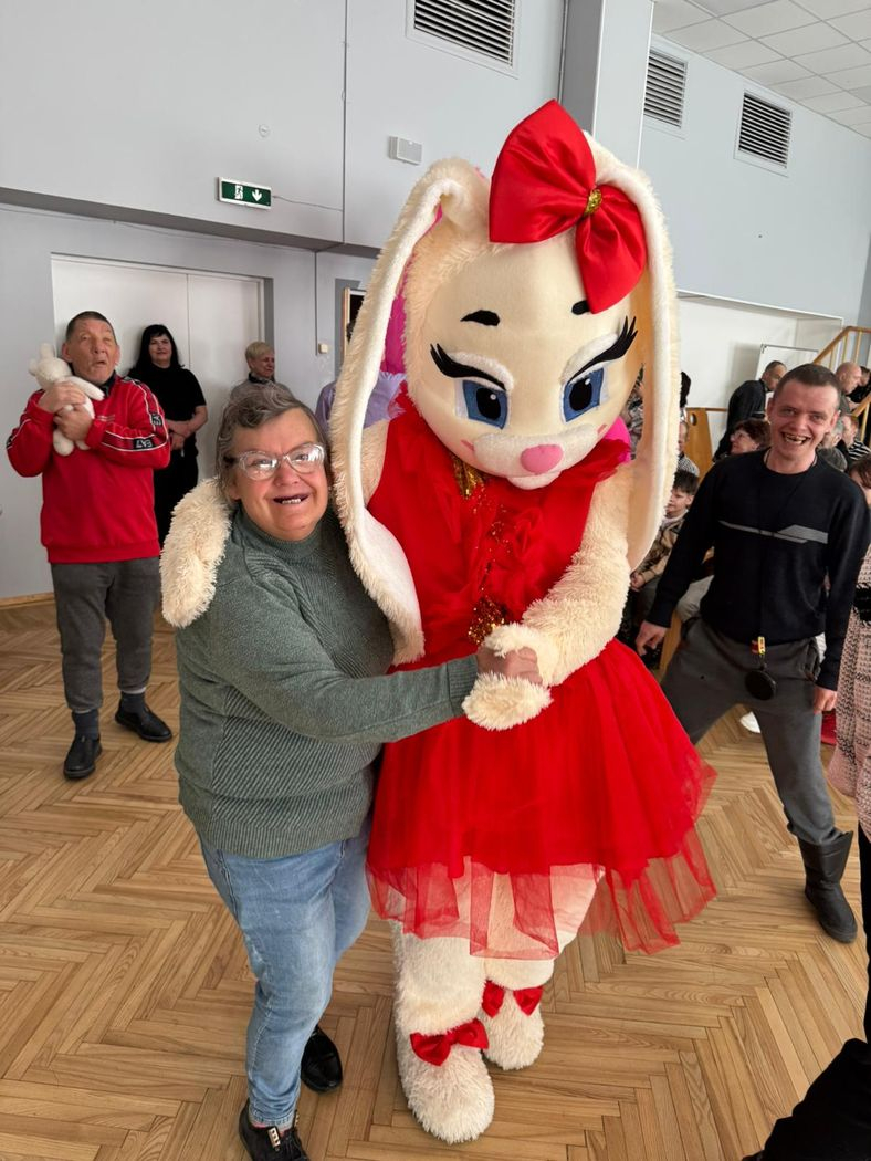 Smaidīga sieviete apskauj cilvēku lielā zaķa tērpā