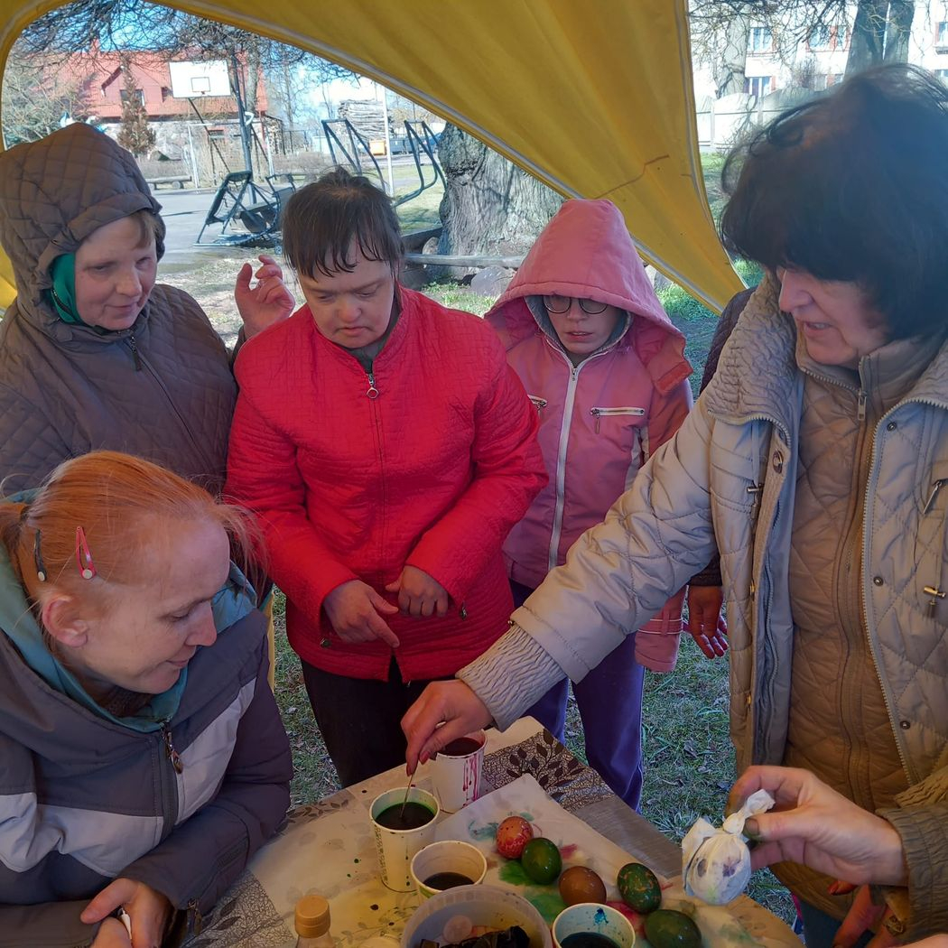 Pieci cilvēki stāv ap galdu un krāso olas