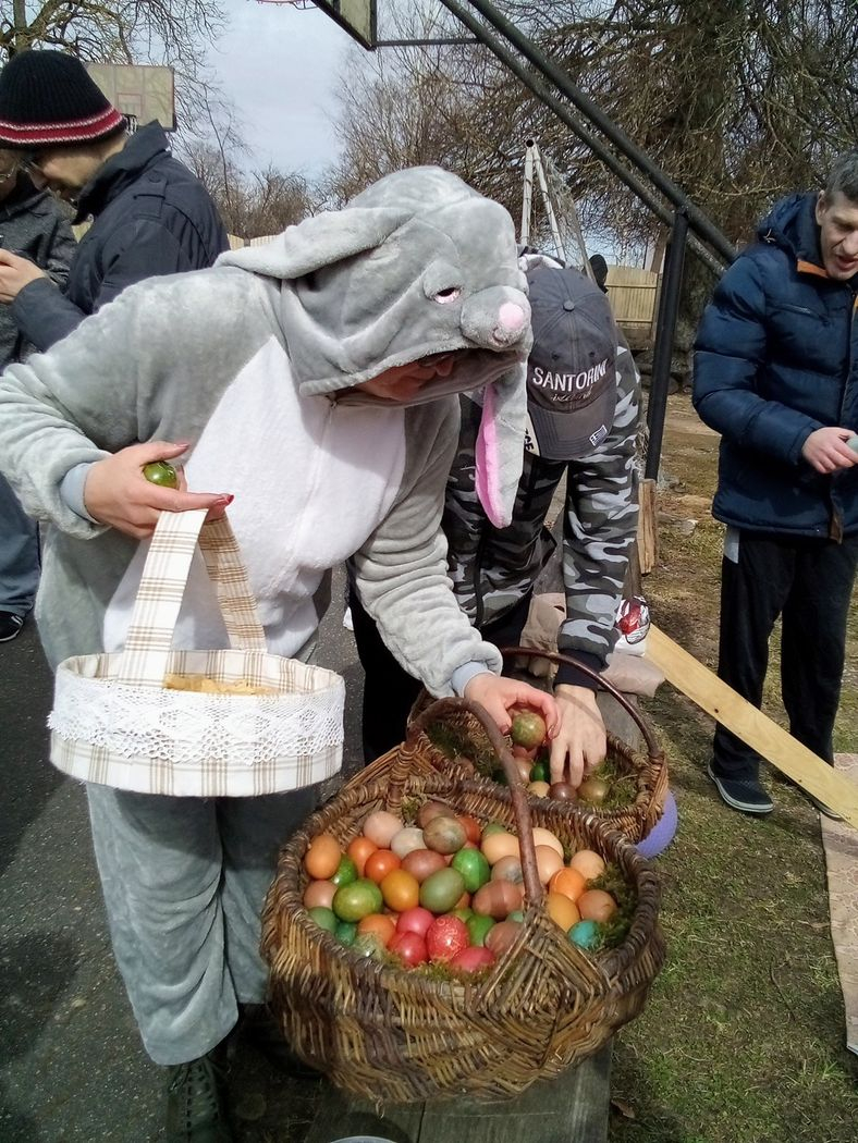Cilvēks zaķa kostīmā ņem no lielā groza krāsotas olas