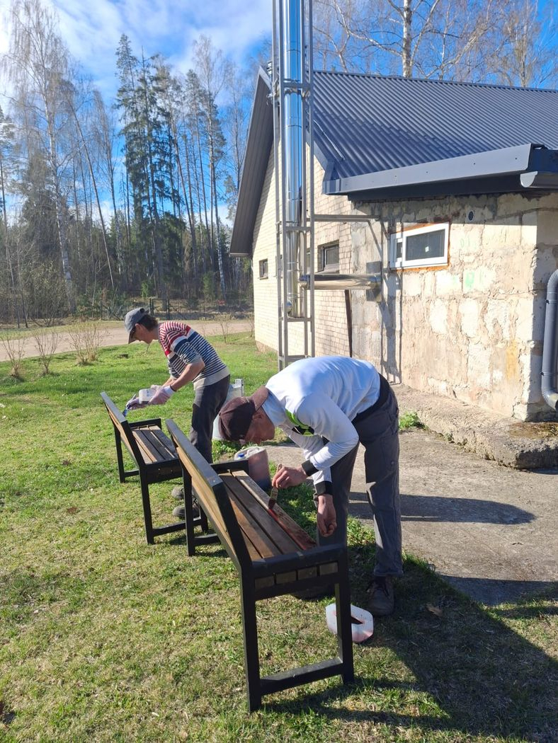 Cilvēki veic teritorijas uzkopšanas darbus. Krāso soliņus