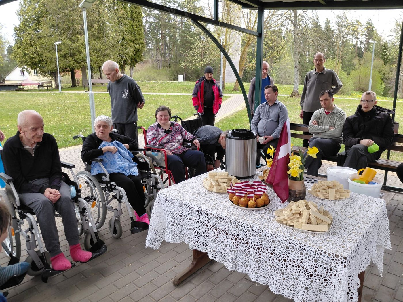 Cilvēki nojumē pie klāta galda