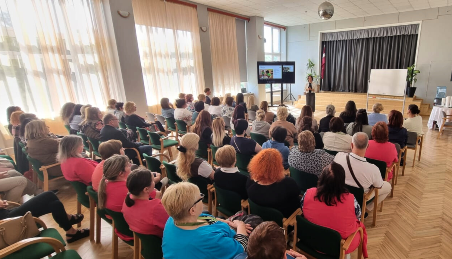 Zāle pilna ar dalībniekiem, kuri klausās runātājā