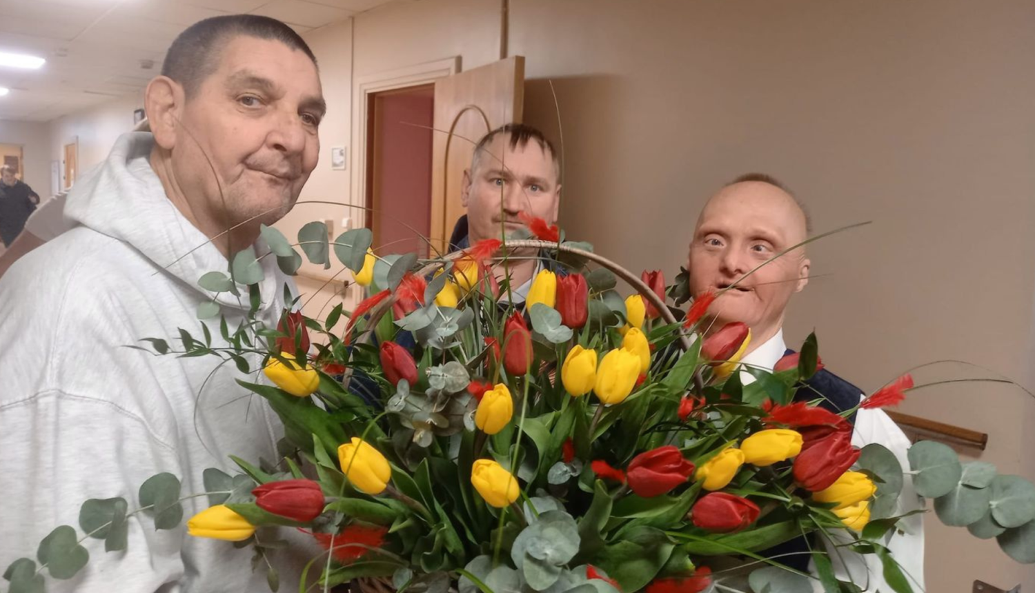 Trīs iedzīvotāji vīrieši tur grozu pilnu ar dzeltenām tulpēm