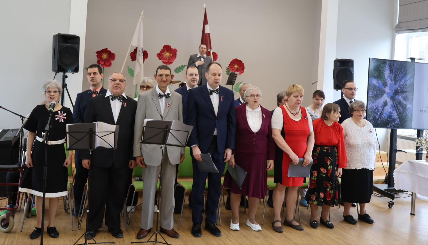 Iedzīvotāju ansamblis. Dziedātāji stāv uz skatuves un izpilda dziesmu.
