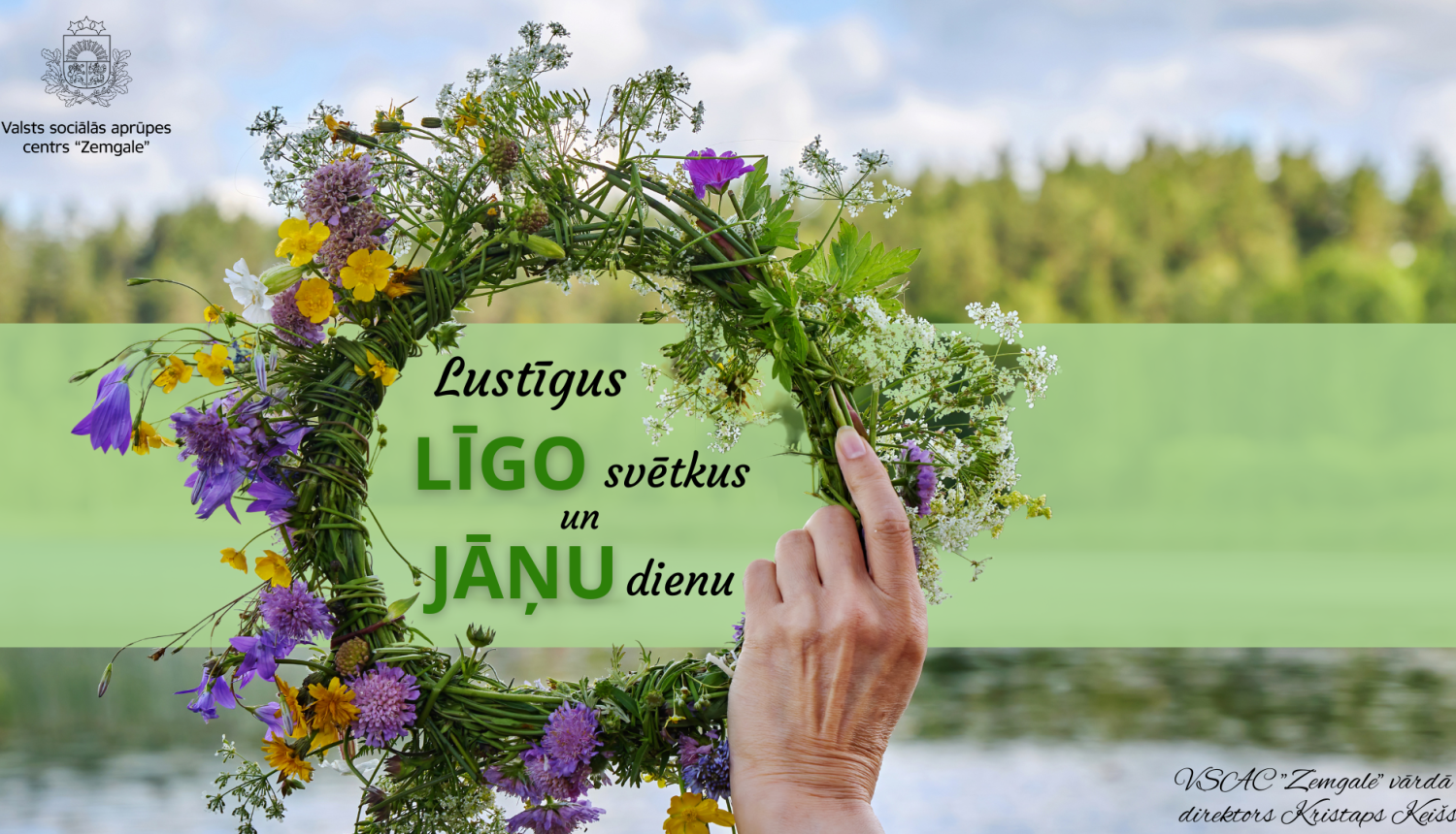 Apsveikumā dabasskats un roka, kas tur vainagu sapītu no pļavas puķēm. Uzraksts lustīgus līgo svētkus un Jāņu dienu