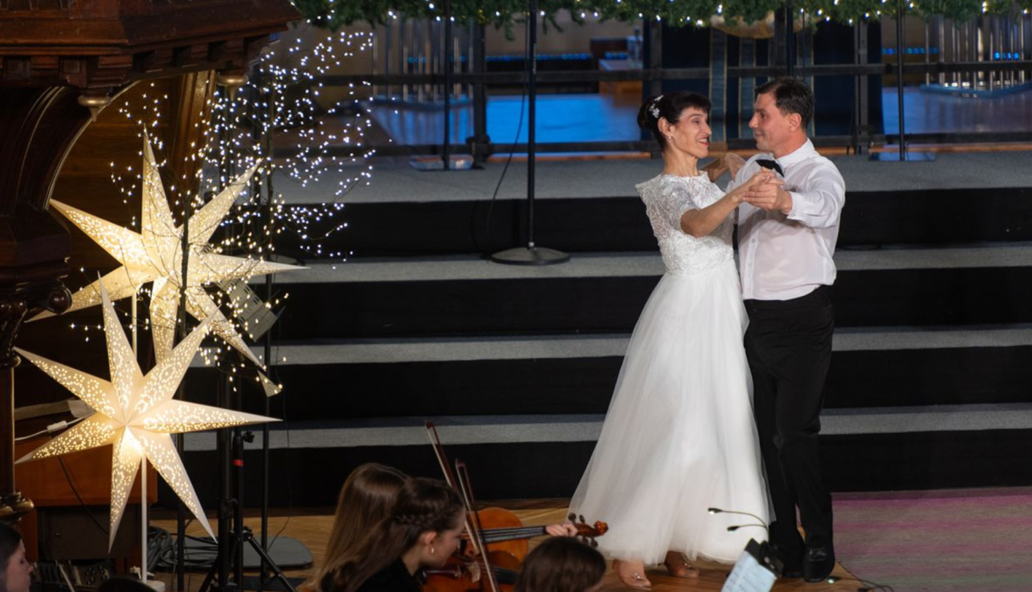 Dejotāji baltajos tērpos baznīcā. Redzamas skaistas lielās zvaigznes.