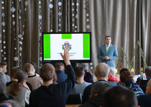 Zālē sēž iedzīvotāji, priekšā iestādes direktors vada kopsapulci