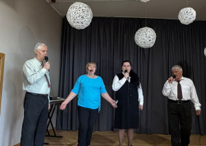 Uz skatuves ar mikrofoniem uzstājasčetri cilvēki